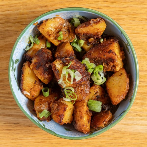 Close-up of Cafe 26's crispy roasted potatoes topped with fresh green onions in a blue bowl.