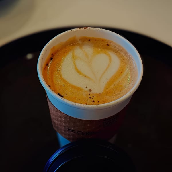 A Cafe 26 latte with heart-shaped latte art in a disposable cup.