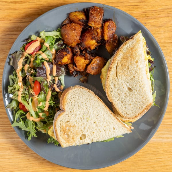 A Cafe 26 breakfast plate with a sandwich, roasted potatoes, and a side salad.