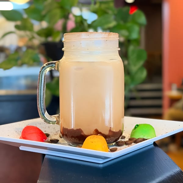 Iced coffee in a mason jar with chocolate syrup, coffee beans, and colorful candies on a white plate.