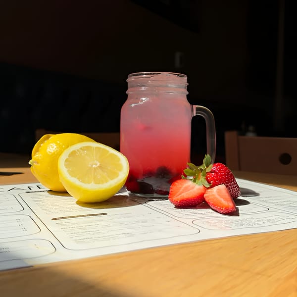 Pink berry lemonade in a mason jar with lemons and strawberries on a Cafe 26 menu.