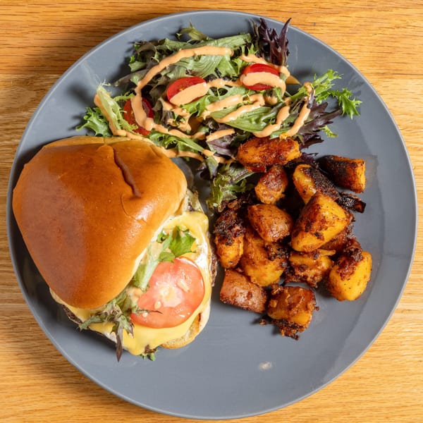 Cafe 26 burger with melted cheese, tomato, lettuce, a side salad, and roasted potatoes.