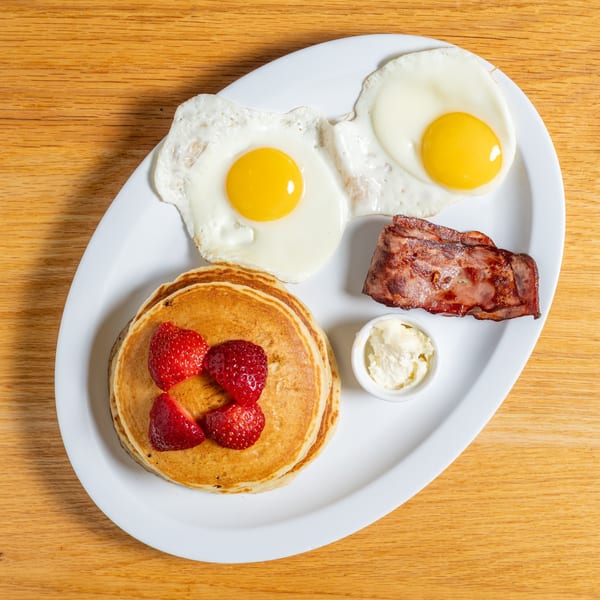 Cafe 26 breakfast plate with pancakes, strawberries, bacon, two fried eggs, and butter.