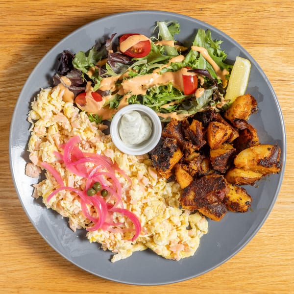 Cafe 26 breakfast plate with scrambled eggs, roasted potatoes, mixed greens salad, and dipping sauce.