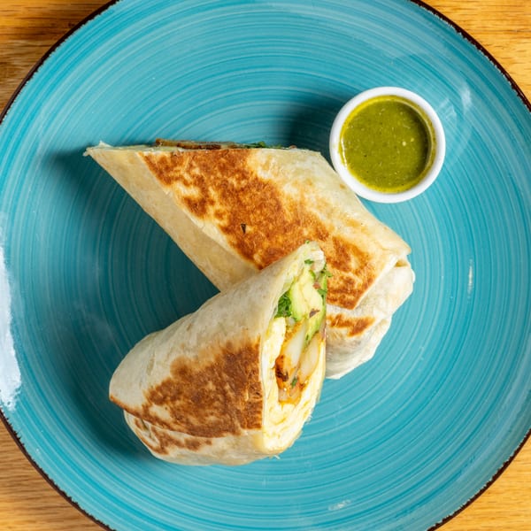 Two Cafe 26 burritos, one cut open to show avocado and shrimp, with green sauce on a blue plate.