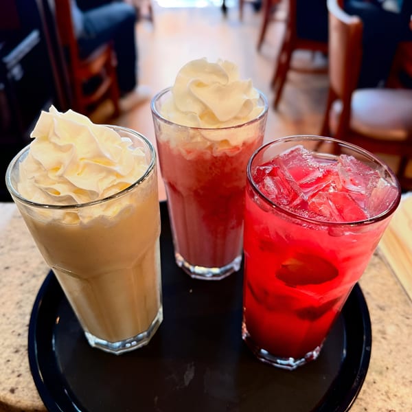 Three colorful Cafe 26 drinks: a yellow smoothie, a pink smoothie, and a red iced drink.